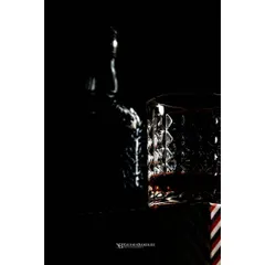 This is a study in light and glass. The focus is entirely on the way light catches the textured pattern of the whiskey glass, with the bottle as a subtle silhouette in the background. It’s dark, moody, and full of texture.