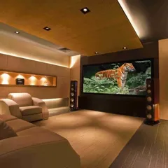 This home theater uses warm wood tones and recessed lighting to create a cozy yet sophisticated ambiance, complemented by a large screen and powerful floor-standing speakers.