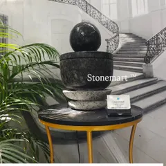 A modern tabletop fountain carved from granite. The piece features a dark granite sphere and bowl, resting on a lighter granite base, creating a beautiful contrast.