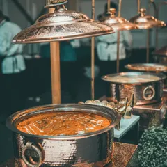A rich Indian curry in a traditional hammered copper pot, part of an elegant buffet setup.