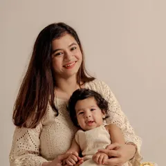 A sweet mother and baby portrait taken to celebrate a six-month milestone. The coordinated cream-colored outfits and the soft, neutral background create a warm and gentle image.