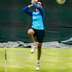 A bowler in mid-action, showcasing a classic high-arm delivery. This form generates bounce and pace, making it difficult for the batsman.
