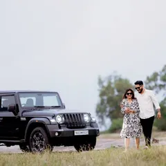 A duplicate of the first image, showing a stylish couple walking hand-in-hand next to a black Mahindra Thar in a rustic, open landscape.
