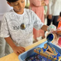 A young boy carefully pours layers of blue and yellow paint, watching as the colors merge and create incredible patterns on his wooden letter.