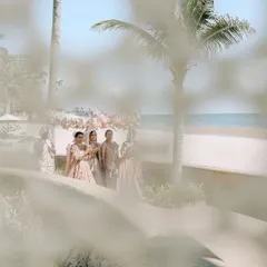 A dreamy, through-the-foliage shot of the bride's family waiting by the beach in Thailand. This artistic framing creates a sense of anticipation and place.