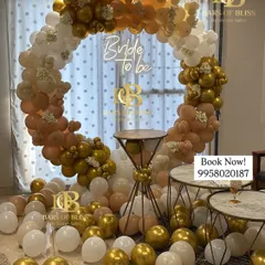 A classic 'Bride to be' setup for a bachelorette party or bridal shower. The decor features a full ring of white, peach, and gold balloons, with a neon sign and a pedestal for the cake.