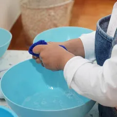 A child learns to wash with a sponge and water. This practical life activity teaches a multi-step process, develops motor skills, and instills a sense of care for one's environment.