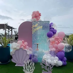 A beautiful mermaid theme birthday decoration set against a poolside lawn. I used a shimmer wall backdrop, a pastel balloon garland in pink, purple, and white, and custom props like a large seashell and coral cutouts.