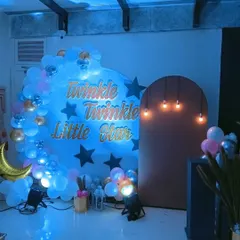 A closer view of a "Twinkle Twinkle Little Star" baby shower backdrop, featuring blue back-lighting and hanging Edison bulbs for a warm glow.