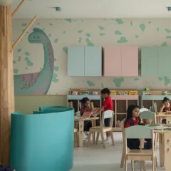 Pastel-colored storage cabinets and a dinosaur mural in the nursery library. This area provides a space for more structured activities like drawing or group reading, complementing the free-form play zones.