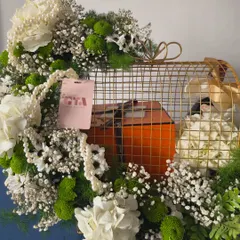 A closer look at the golden birdcage hamper, showing the intricate details of the cage and the lush arrangement of white and green florals surrounding the luxury gift.