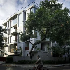 The Boat Club Apartments viewed from the street, nestled amongst mature trees. The design aims to be a respectful addition to the neighborhood, balancing modern aesthetics with a connection to its natural context.