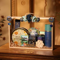 This premium Diwali hamper comes in a wooden crate with a clear acrylic lid, beautifully decorated with floral accents. It's filled with gourmet snacks, sweets, and traditional items.