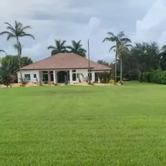 The completed exterior of a modern farmhouse. The design features a tiled roof, large arched entryways, and an expansive lawn, creating a serene and impressive property.