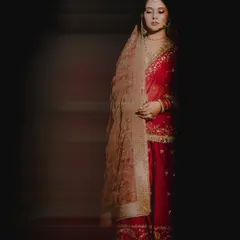 A moment of quiet contemplation for the bride. The dramatic lighting highlights her traditional red attire and the serene expression on her face before the ceremony.