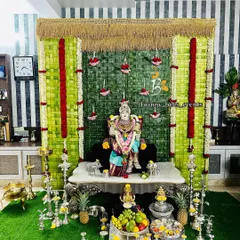 A complete puja setup featuring our signature woven coconut leaf backdrop. This Varamahalakshmi decoration combines the natural green panel with floral hangings and traditional silver puja items for a truly authentic feel.