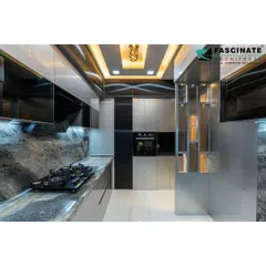 This ultra-modern kitchen in Seawoods features sleek, metallic-finish cabinets and a stunning grey marble-patterned backsplash that extends up the wall. A decorative ceiling with a gold-finish light fixture adds a luxurious final touch.