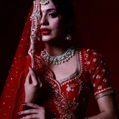 A direct and powerful bridal portrait. The bride looks straight at the camera, her expression confident, with the rich red of her lehenga creating a bold statement.