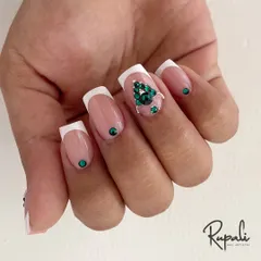 A classic French manicure gets an upgrade with a stunning emerald green Swarovski crystal tree design. This is a perfect example of festive or holiday nail art.