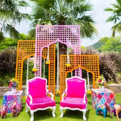 A perfect photo spot for the bride and groom. This seating area featured bright pink chairs set against a backdrop of orange and pink jaali panels, embodying the colorful spirit of a Rajasthani carnival.