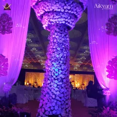 A massive floral pillar made entirely of white and purple flowers, creating a dramatic and luxurious statement piece within a large reception hall.
