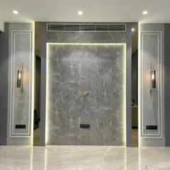 This drawing room wall features a grey marble-finish panel with dramatic backlighting. Flanked by modern wall sconces, this design creates a symmetrical and highly sophisticated focal point.