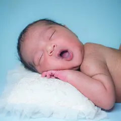 That tiny yawn. Moments like these are so fleeting, which is why I work patiently to capture them. This little one is resting on a soft pillow against a simple blue backdrop.