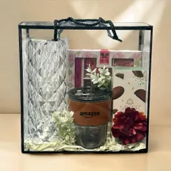 This modern Diwali gift set for Amazon is presented in a clear acrylic box, showcasing a crystal-cut vase, a branded tumbler, and other elegant treats.