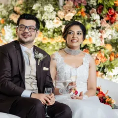 The happy couple enjoying their wedding reception. The lush, multi-colored floral wall behind them adds a vibrant and celebratory feel to their candid photos.