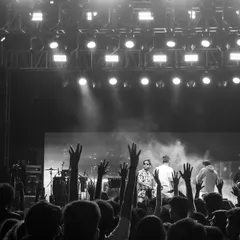 A black and white perspective from the back of the venue, focusing on the audience's participation with hands raised in the air, creating a powerful, timeless concert image.
