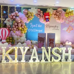A grand stage setup for a teddy bear themed first birthday party, complete with large marquee letters spelling out the name 'KIYANSH' and multiple themed backdrops.