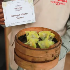 Our Asparagus and Water Chestnut Dimsum, presented by a server in a bamboo steamer. These vegetarian dumplings are a light, healthy, and delicious option.