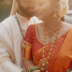 A sun-kissed, romantic close-up of a South Indian couple, focusing on the bride's stunning temple jewelry.