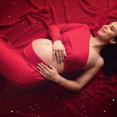 A moment of pure bliss. This artistic top-down shot on a bed of red fabric captures the serene joy of pregnancy. The scattered gold glitter adds a touch of magic.