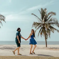 A classic romantic walk on the beach, with the couple hand-in-hand against the backdrop of the sea and palm trees.