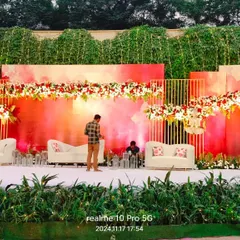 A modern and artistic reception stage setup at The Acres Club. The watercolor-style backdrop in shades of pink and red, paired with clean white sofas, offers a contemporary and vibrant look.