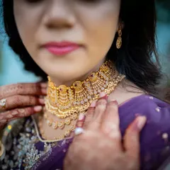 A detailed shot focusing on the bride's elegant gold necklace and the beautiful henna patterns on her hands.