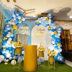 A bright and cheerful birthday decoration in a home setting. This setup uses a blue, white, and gold color palette with dual arched backdrops, a neon sign, and floral accents.