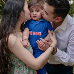 A proud family moment with parents kissing their little one, who is dressed in a tiny "India" cricket jersey. A perfect shot from a fun, outdoor family session.