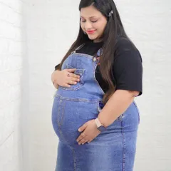 A simple and beautiful profile shot showcasing the baby bump. The denim overalls provide a casual and modern look for this relaxed studio maternity photo.
