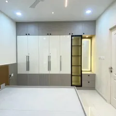 This custom wardrobe combines glossy white shutters with grey panels and fluted detailing for a modern, two-tone look. I integrated a backlit dressing mirror and open display shelves, providing both concealed storage and a place to showcase personal items.
