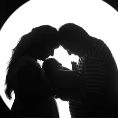 A powerful and artistic silhouette of new parents adoring their newborn. This black and white newborn portrait focuses on the emotion and bond of a new family.