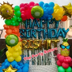 A vibrant Pool Party theme for a terrace celebration. The decor features a bright, multi-colored balloon arch, a shimmer backdrop, and fun foil balloons like a smiling sun, kiwi, and pineapple.