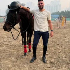 A rider poses proudly with his horse after a great session, with the horse playfully wearing the helmet.