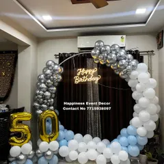Even in a smaller space, a balloon ring can make a big impact. This setup for a 50th birthday was done at home, featuring a silver, white, and blue balloon arch with a neon sign and foil number balloons.