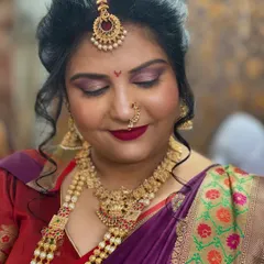A close-up of a South Indian bridal makeup look. The focus is on the rich colours of the eyeshadow, the bold lip, and the traditional gold jewellery, including the maang tikka and temple necklace.
