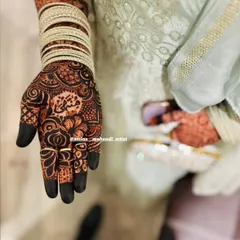 A candid shot of the bride's hand, showcasing the beautiful henna stain and a personalized name in Arabic script.