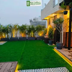A wide view of a completed terrace in Uttam Nagar, showing the artificial lawn, planters with uplighting, and a seating deck.
