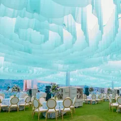 The entire space was transformed with a dreamy, cloud-like ceiling made of flowing pastel blue fabric. This overhead installation complements the Dior-inspired theme and creates a soft, ethereal ambiance for the daytime event.