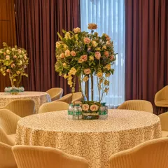 An elegant banquet-style seating arrangement for a corporate conference or luncheon. The tall, cascading floral centerpiece adds a touch of sophistication to the functional setup.